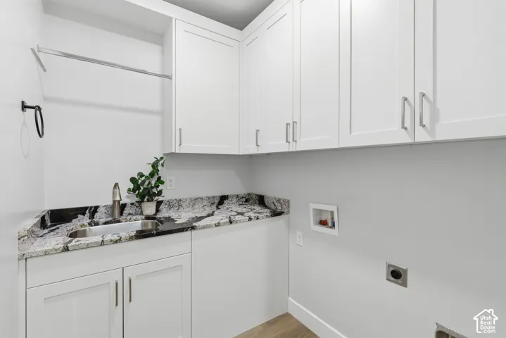 Utility room featuring white shaker cabinetry, patterned stone countertops with an undermount sink, a chrome faucet, and a hanging rod