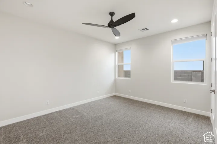 Neutral-toned interior room featuring two windows with roller shades, recessed ceiling lighting, and a dark-toned ceiling fan