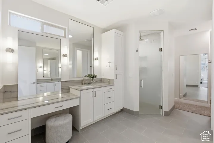 Spacious bathroom featuring a dual vanity, built-in makeup vanity, large rectangular mirrors, and a glass-enclosed shower with a rainfall showerhead