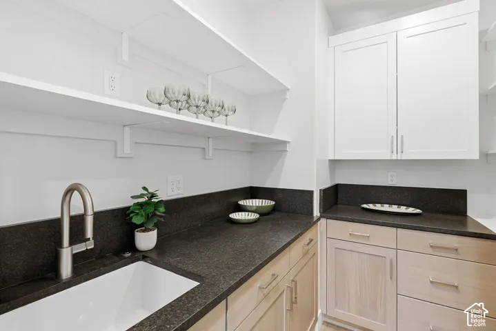 Spacious utility area featuring a deep basin sink with a brushed nickel faucet, dark granite countertops, and light wood-finish lower cabinetry