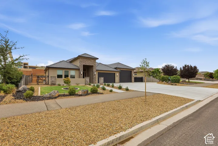 Contemporary stucco exterior featuring stone accents, a multi-car driveway, dark garage doors, a manicured front lawn, and mature landscaping