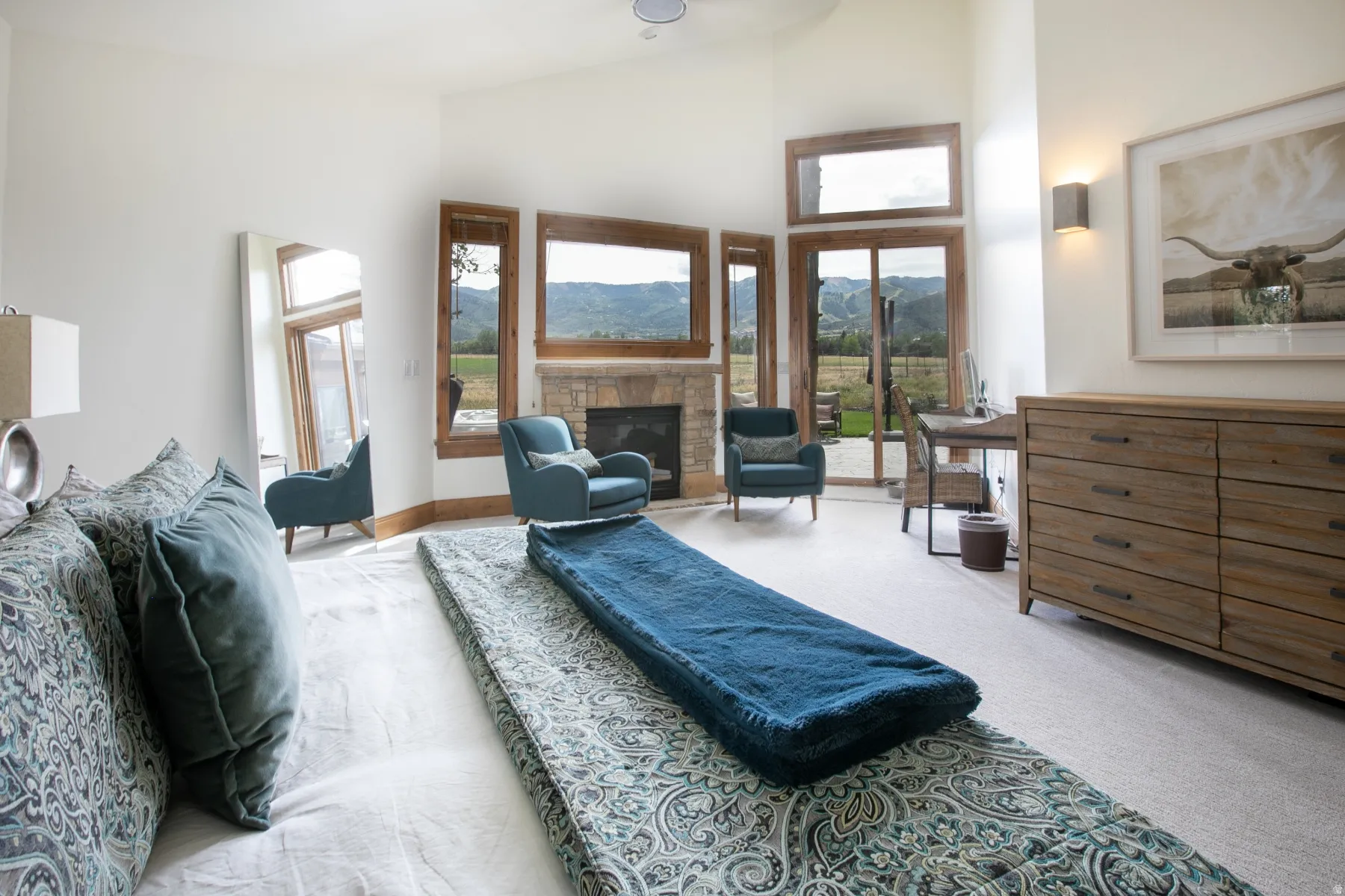 Spacious room featuring vaulted ceilings, a stone fireplace, and multiple floor-to-ceiling windows with wood frames