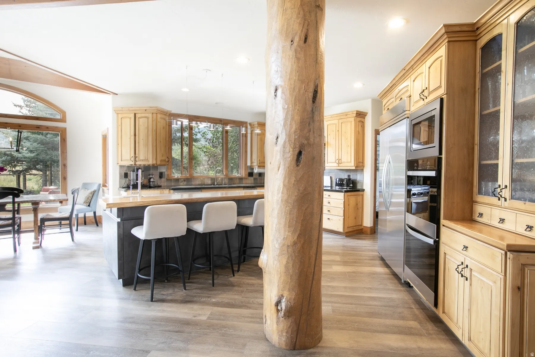 Kitchen featuring light wood cabinetry, a central island with seating, stainless steel appliances, and a natural wood column