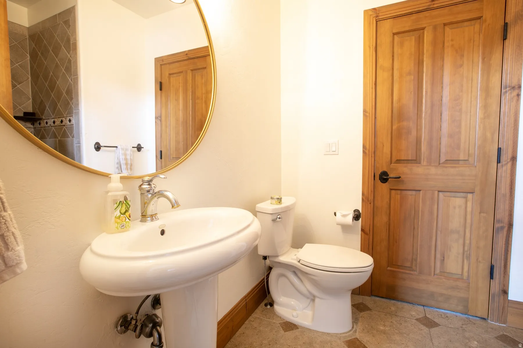 Bathroom featuring a pedestal sink with chrome faucet, a white toilet, and a wood-paneled door