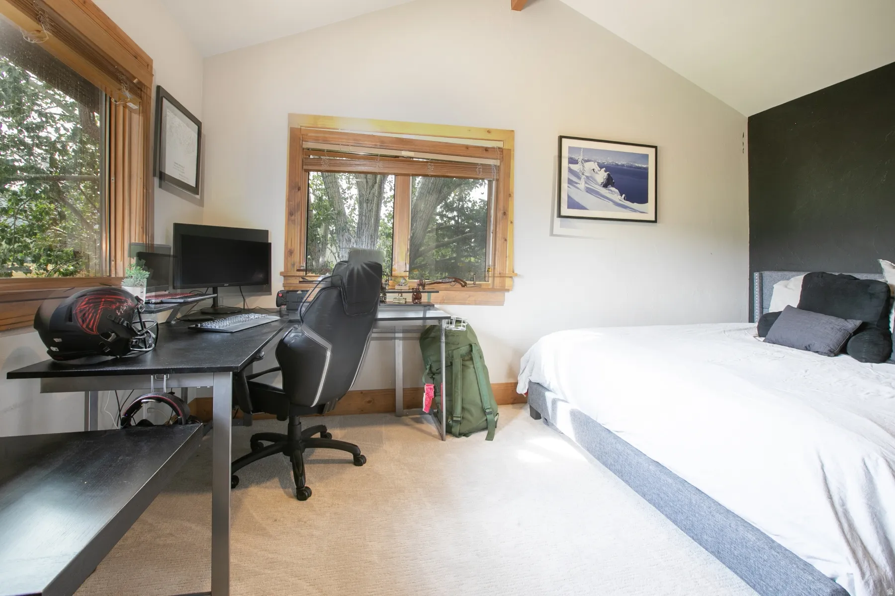 Bedroom featuring wood-trimmed windows, vaulted ceiling, and light-colored carpeting