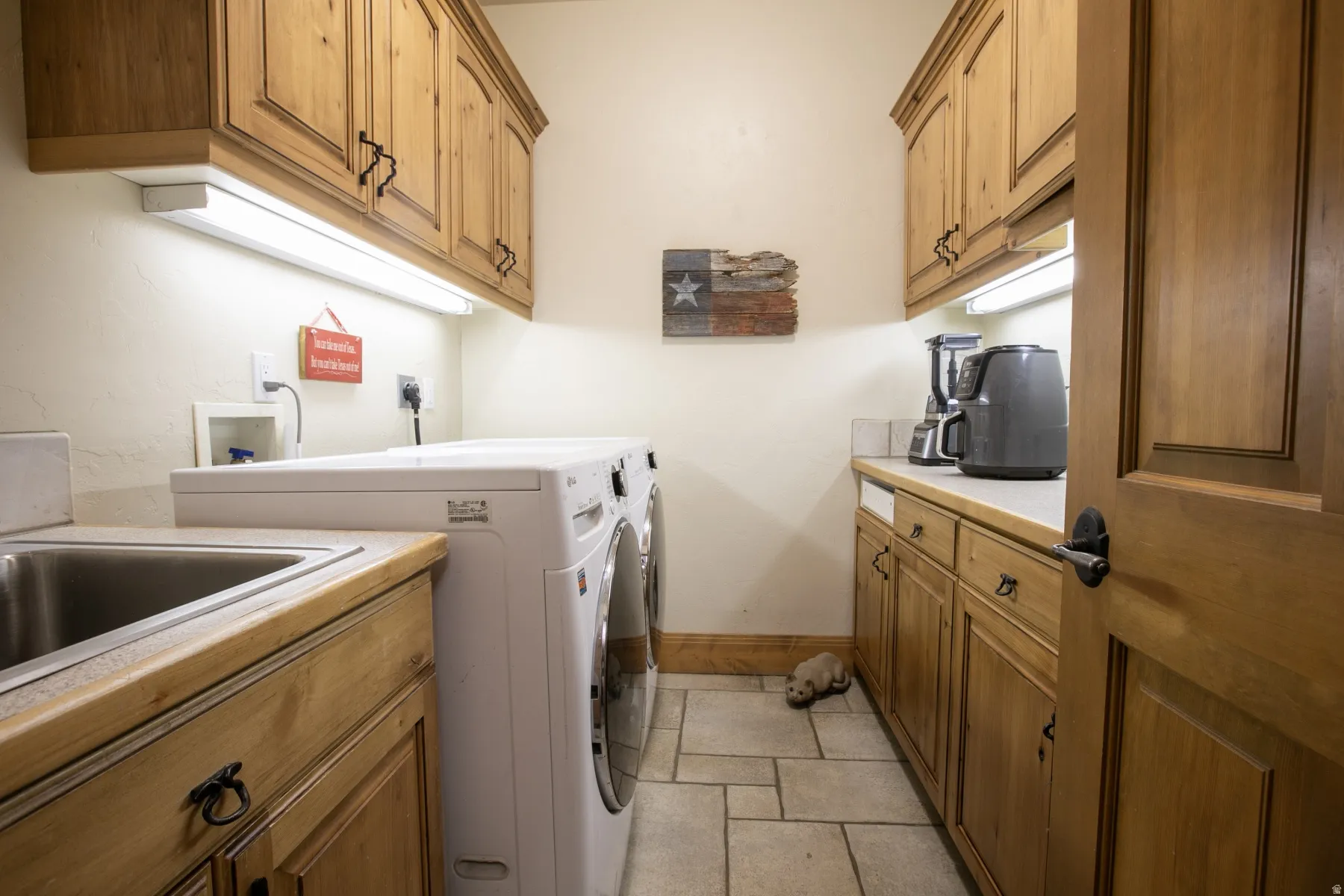Utility room featuring wood-finish cabinetry, under-cabinet lighting, a built-in sink, solid surface countertops, and tile flooring