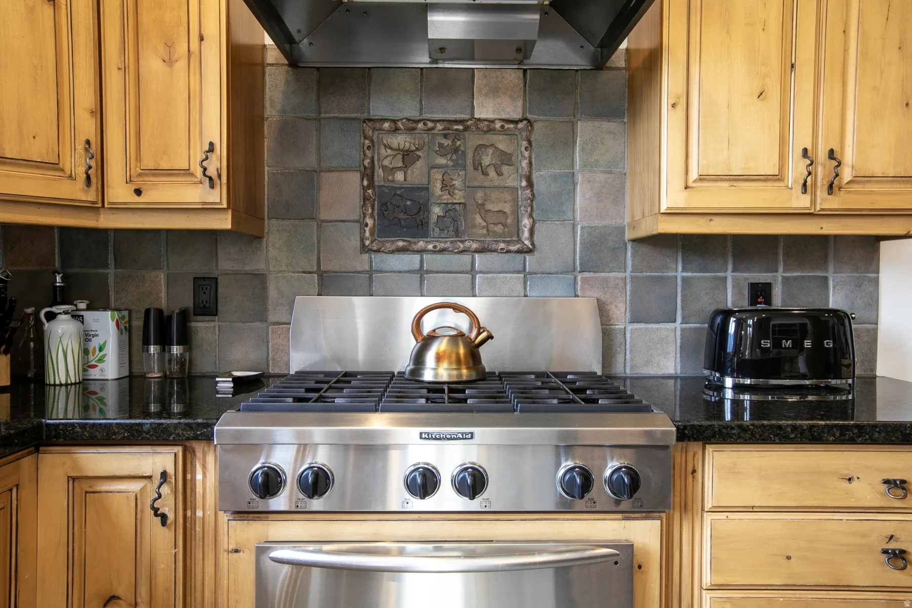 Stainless steel range with a professional-grade hood, complemented by a mosaic tile backsplash and wood-finish cabinetry