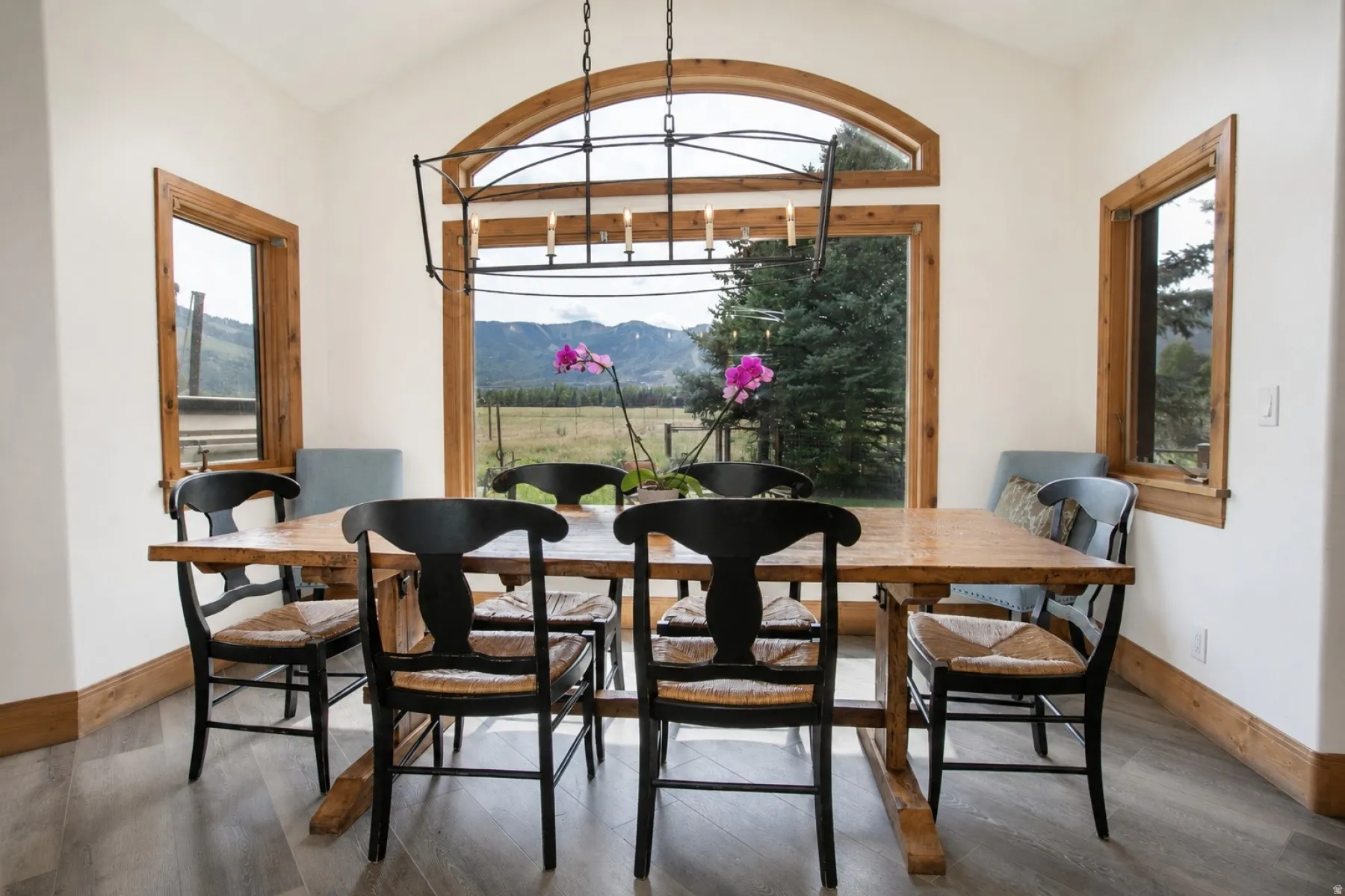 Vaulted ceiling dining area featuring a prominent arched window, wood-finish flooring, and wood window trim throughout