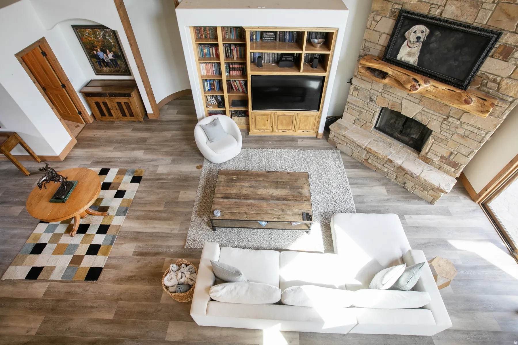 Spacious living area featuring wood-finish flooring, a stone fireplace with a log mantel, and built-in shelving with integrated media storage