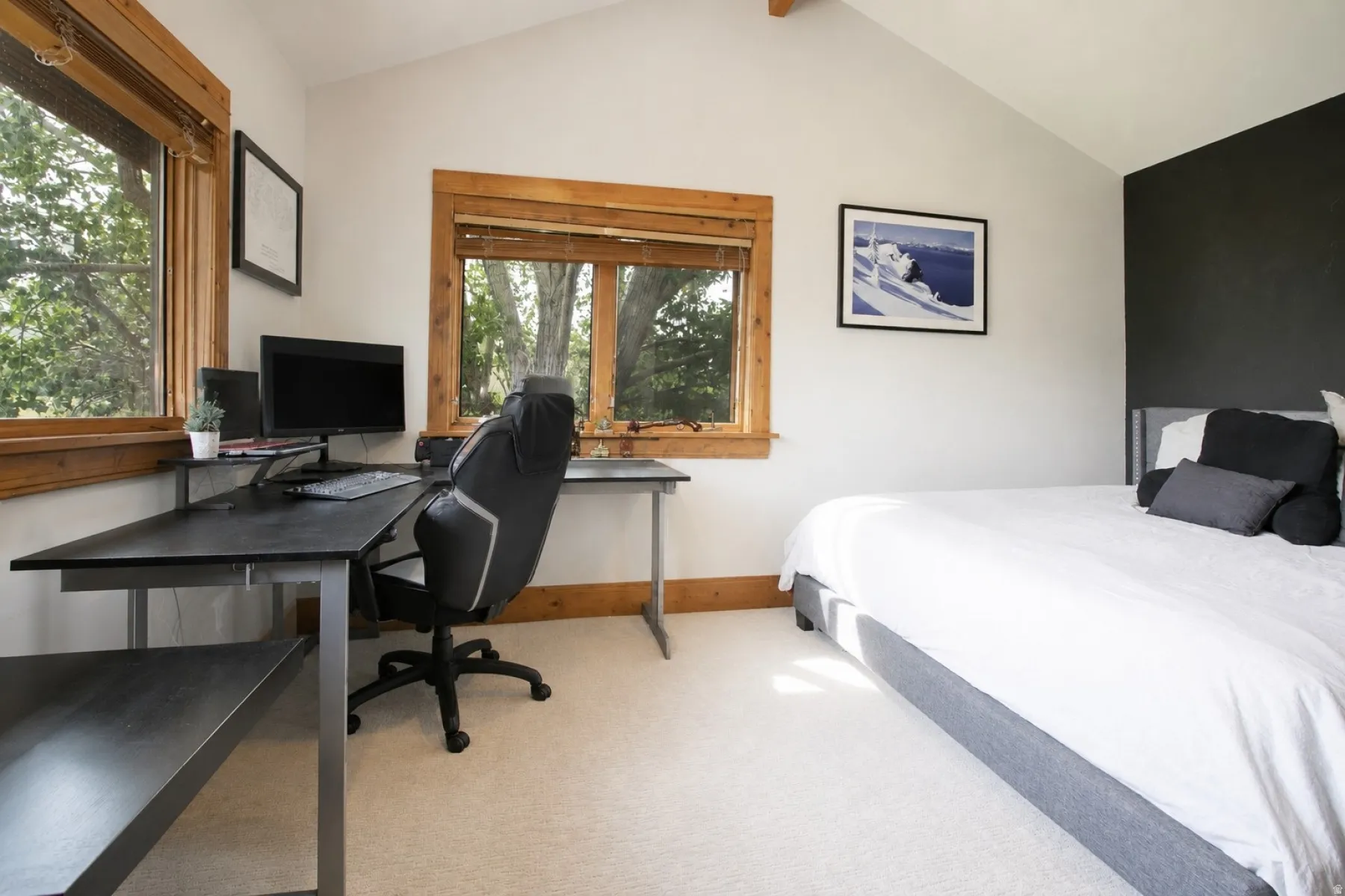 Vaulted ceiling room featuring natural wood window trim, light-toned carpet flooring, a dark accent wall, and multiple windows providing natural light