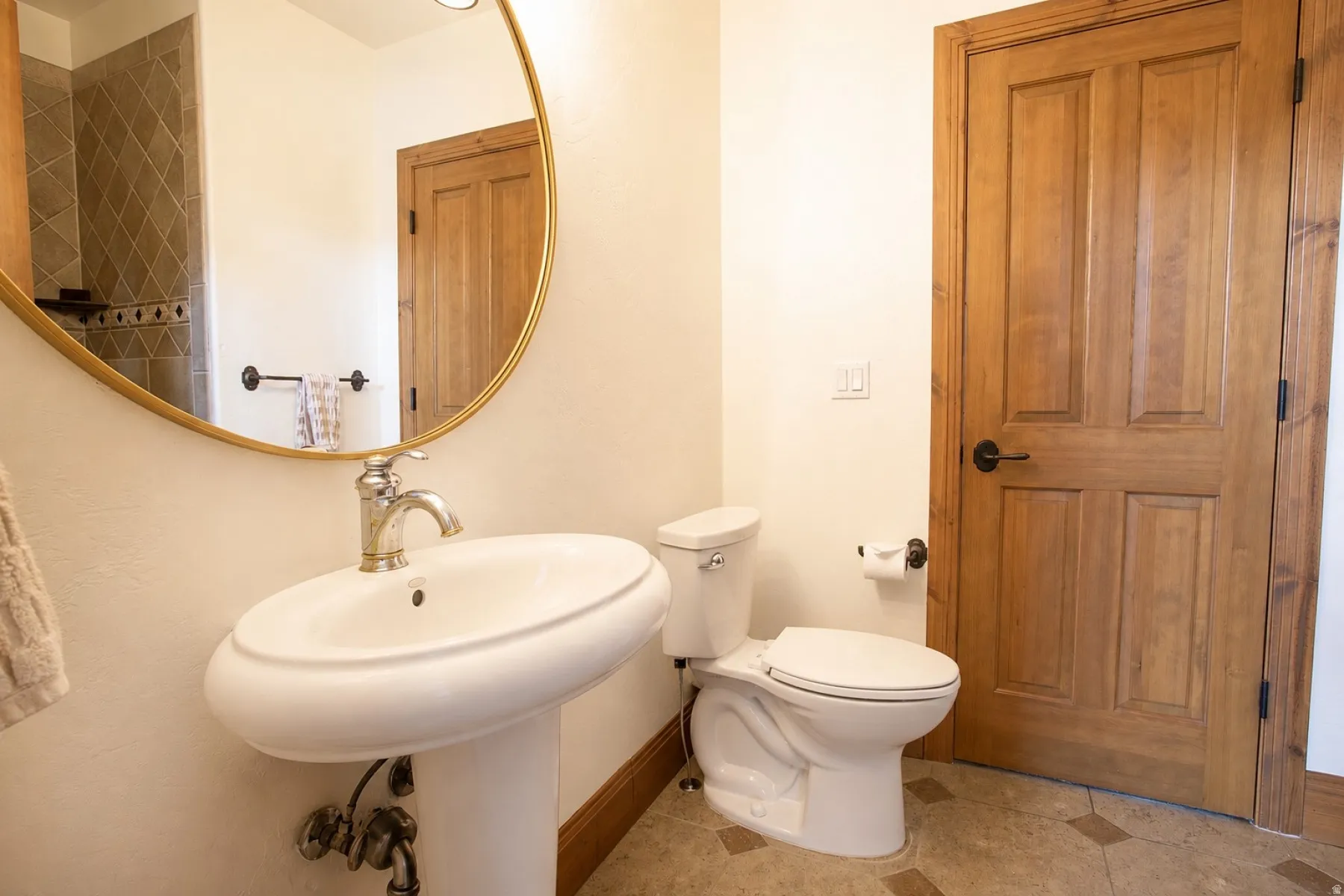 Bathroom featuring a pedestal sink with a chrome faucet, a large round mirror, natural wood panel doors, and tiled flooring