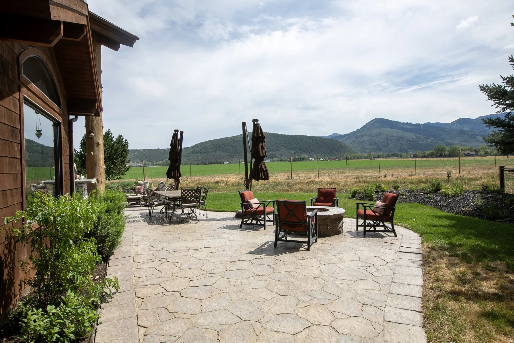 Expansive flagstone patio with a built-in fire pit, bordered by manicured lawn and mature landscaping