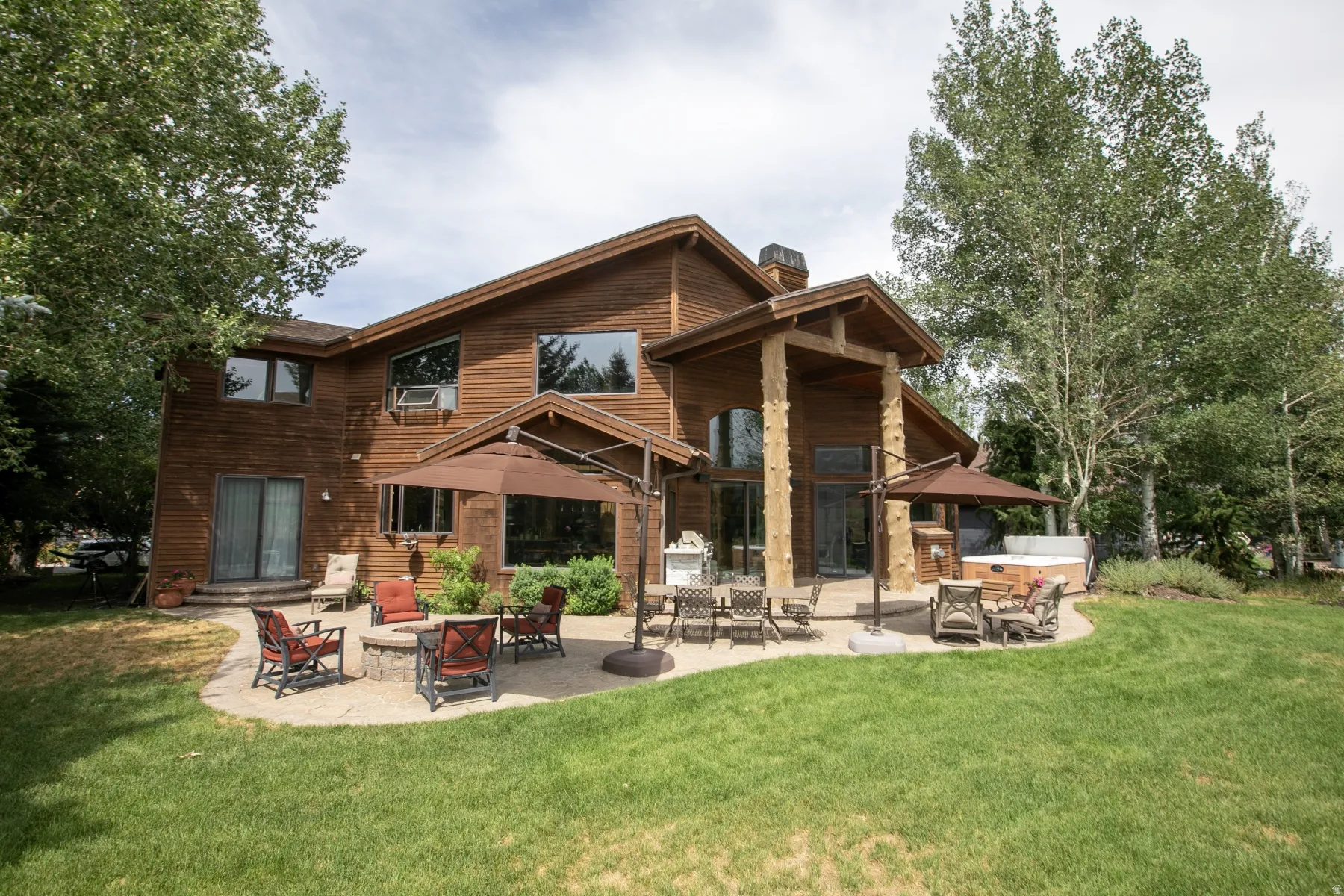 Spacious wood-sided residence featuring an expansive stone patio, integrated fire pit, and outdoor spa