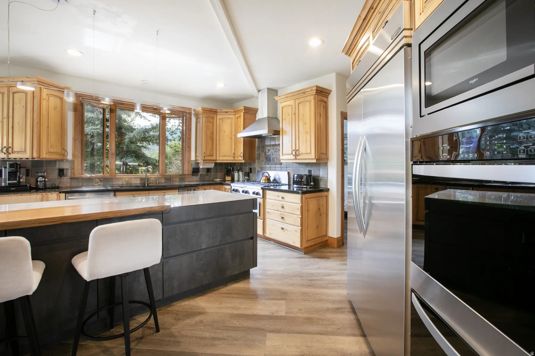 Kitchen featuring wood-finish flooring, natural wood cabinetry, stainless steel appliances, a center island with a light-toned countertop, and a window overlooking exterior trees