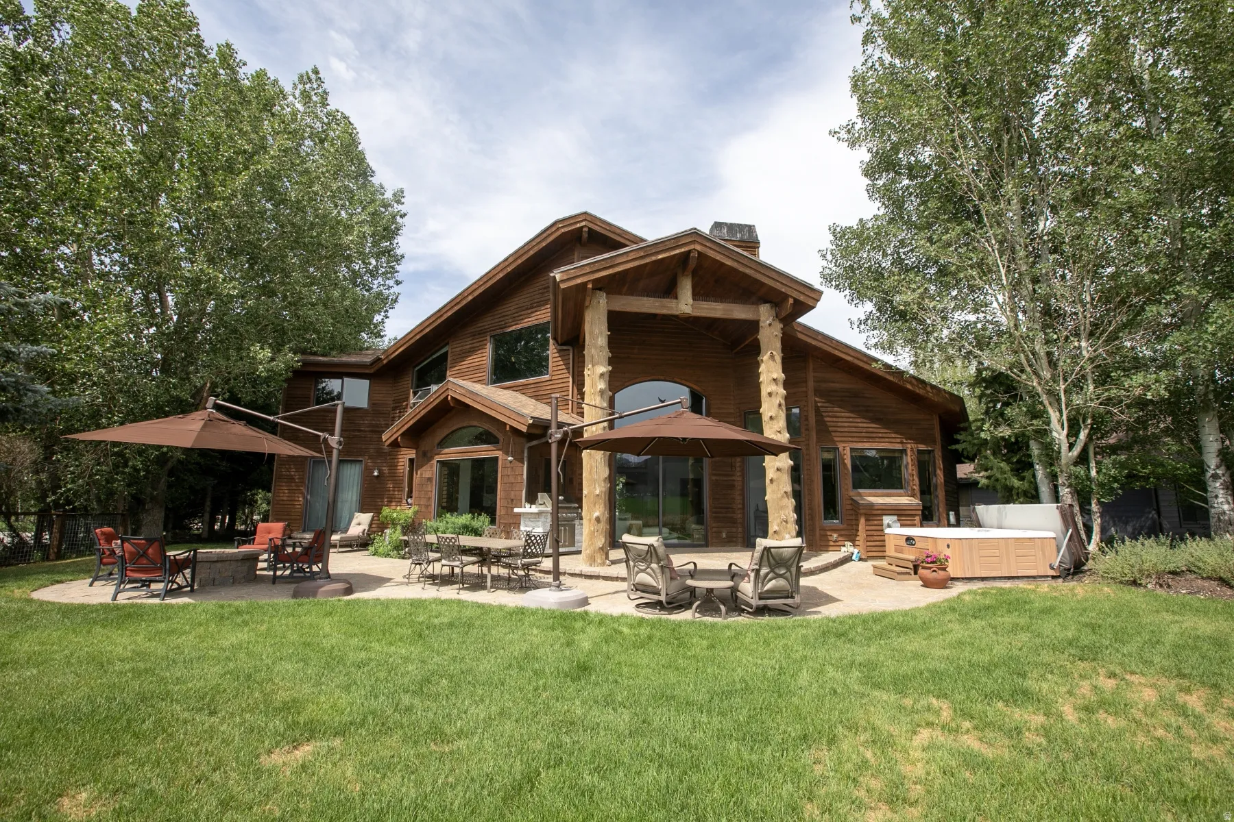 Expansive backyard featuring a manicured lawn, multiple paver patios, and mature trees