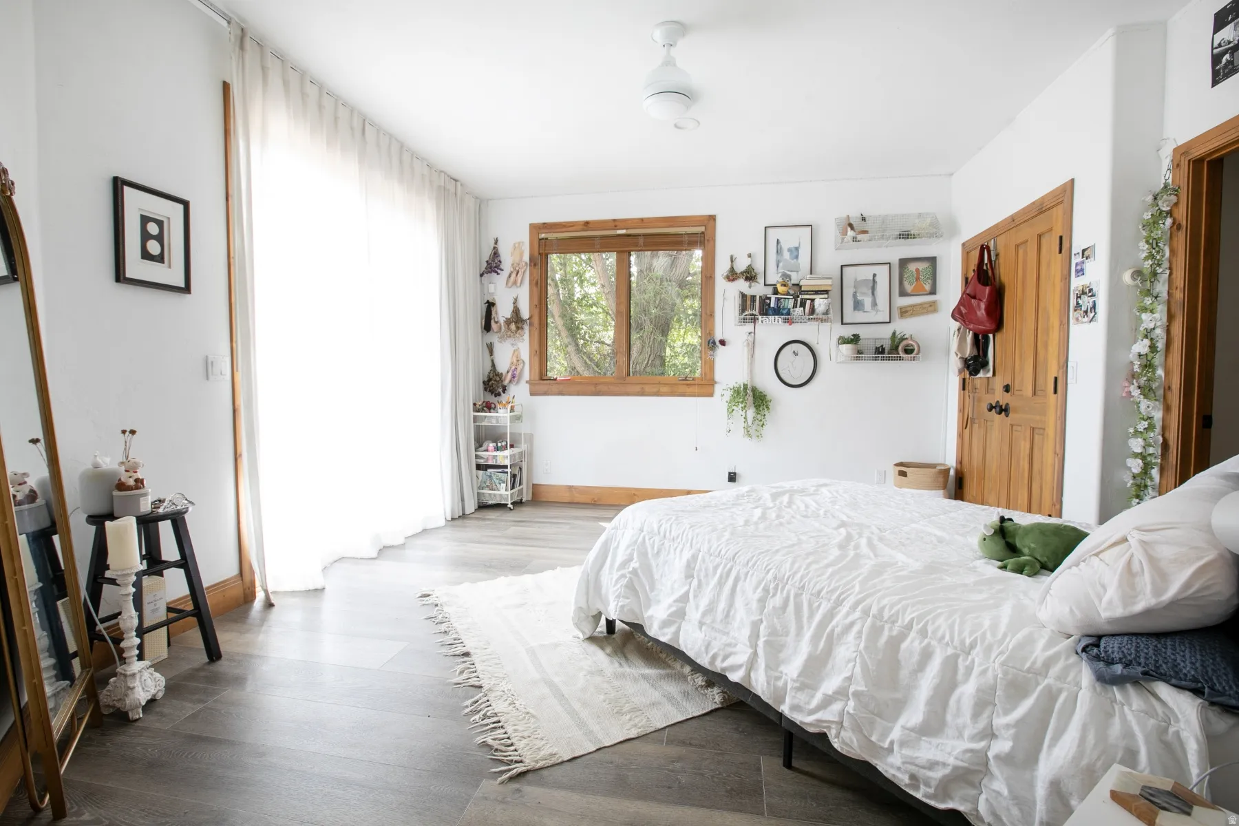 Spacious room featuring wood-finish flooring, a large window with natural wood trim, and a white ceiling fan