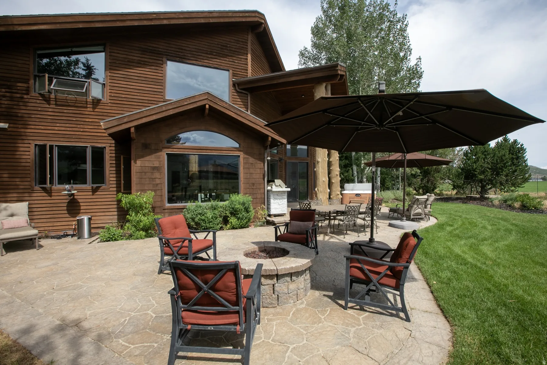 Expansive stone patio featuring a built-in fire pit, multiple seating areas, and a lush green lawn