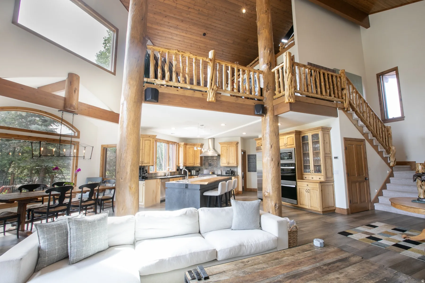 Vaulted living space featuring exposed wood beams, a second-story balcony with natural wood railing, and a grand staircase with carpeted treads