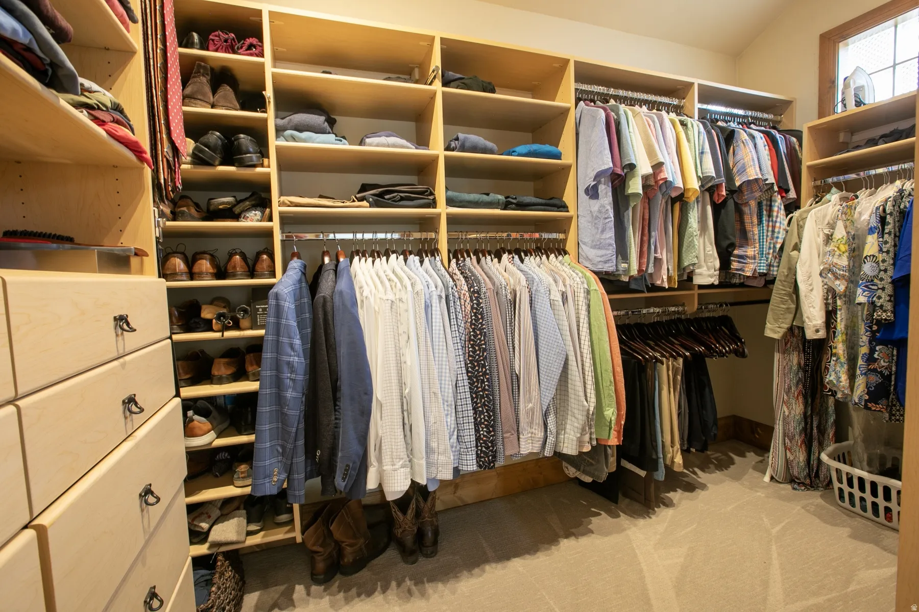 Custom-built closet system featuring light wood-finish cabinetry, integrated shelving, multiple hanging rods, and built-in drawers with dark hardware