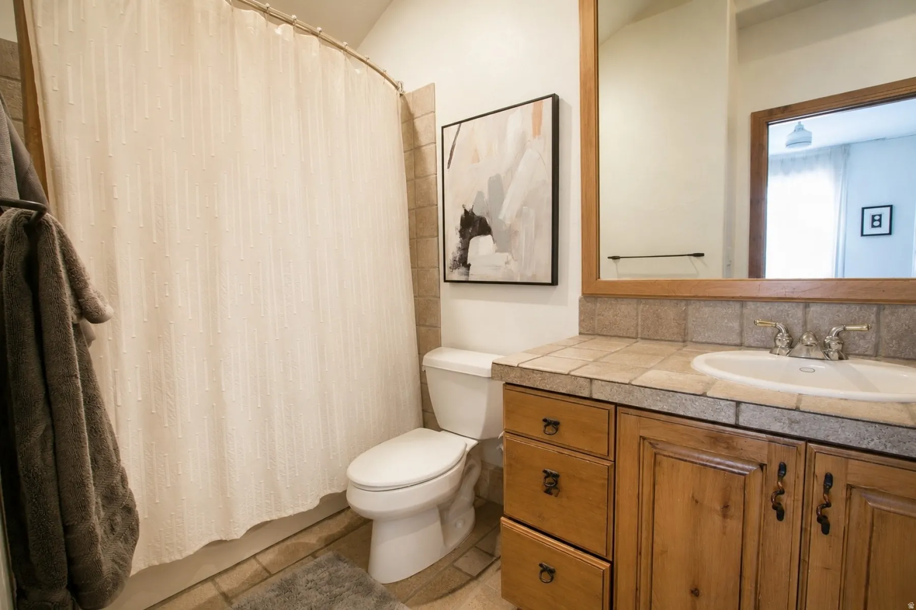 Bathroom featuring a wood-finish vanity with a tile countertop, integrated sink, and wall-mounted mirror