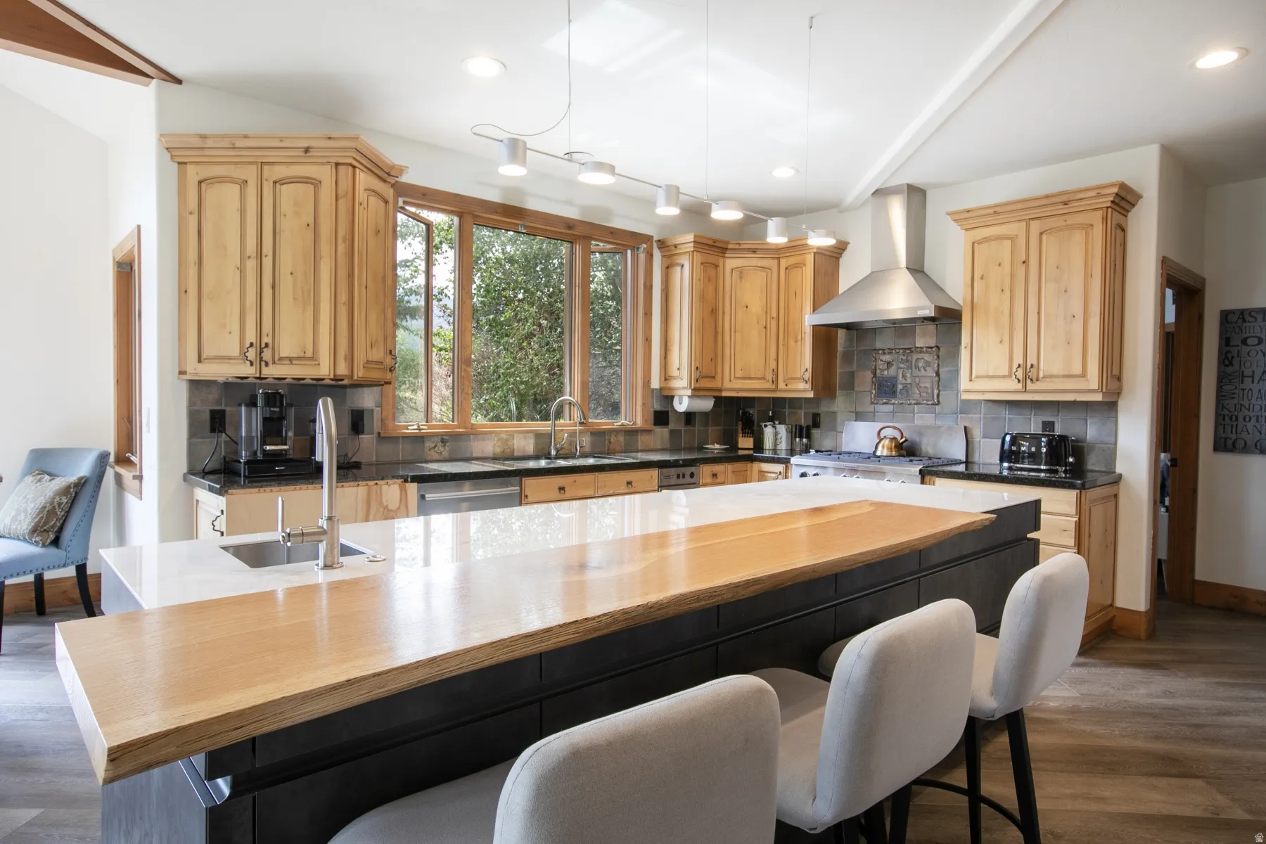 Spacious kitchen featuring light wood cabinetry, a large center island with a wood-finish countertop extension, stainless steel appliances, a tile backsplash, and abundant natural light through multiple windows