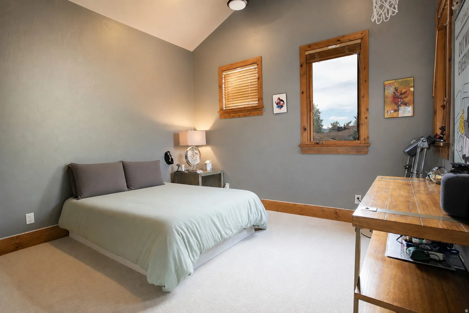 Vaulted ceiling room featuring two windows with natural wood trim, light gray walls, and carpet flooring