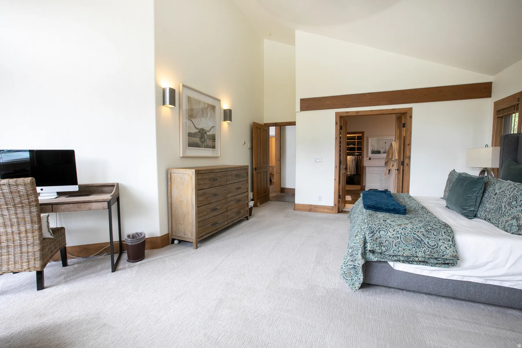 Spacious bedroom featuring light-colored carpet, vaulted ceilings, and natural wood trim