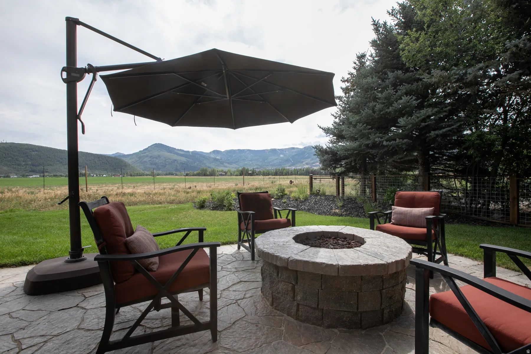 Stoned-paver patio featuring a built-in stone fire pit, bordered by a manicured lawn