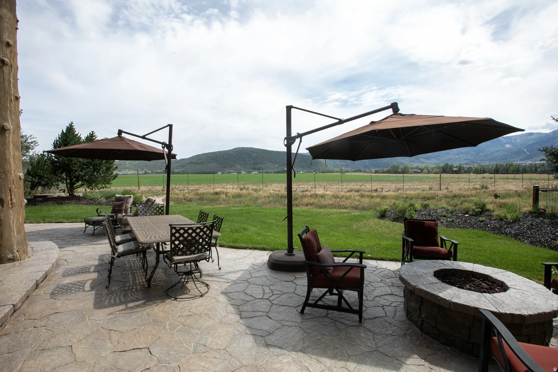 Expansive stone patio featuring a built-in fire pit, multiple seating areas, and direct access to a manicured lawn