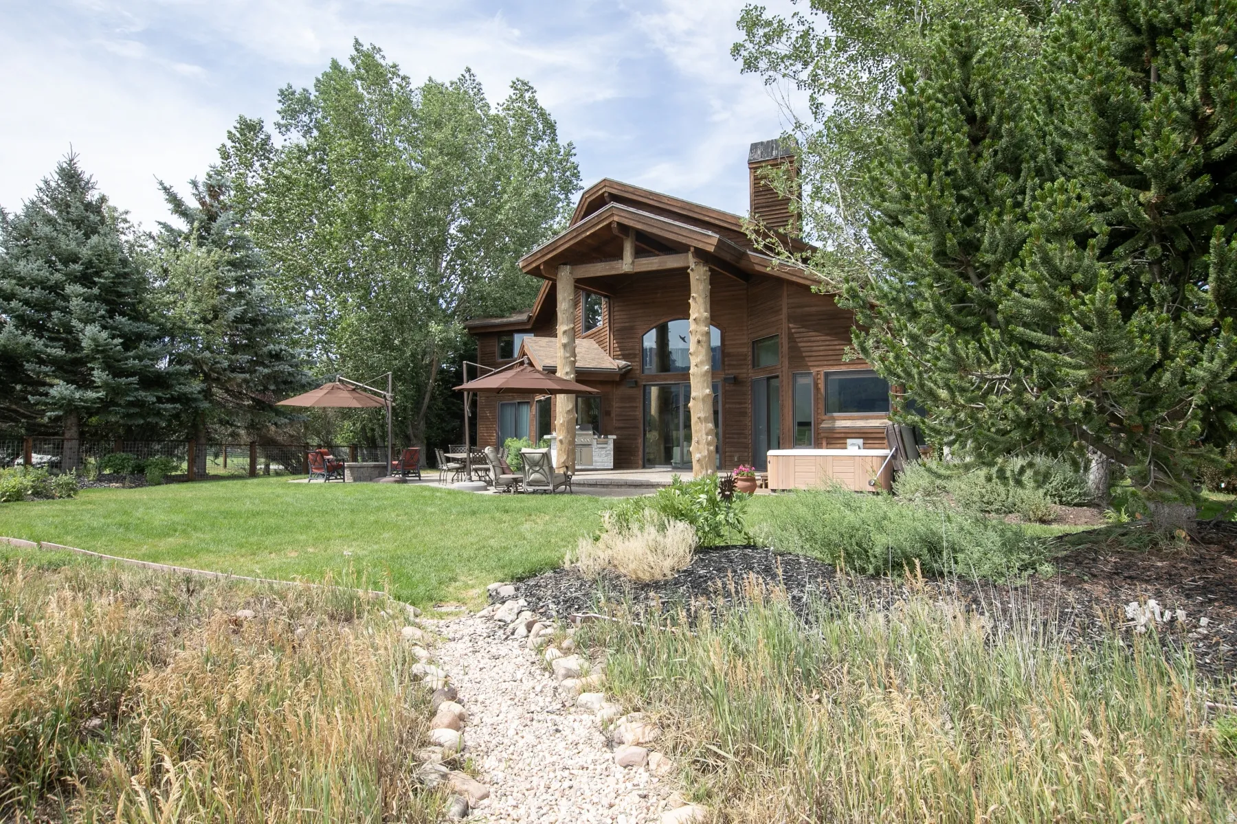 Stunning wood-sided residence featuring a stone chimney, extensive patio space, and a built-in hot tub