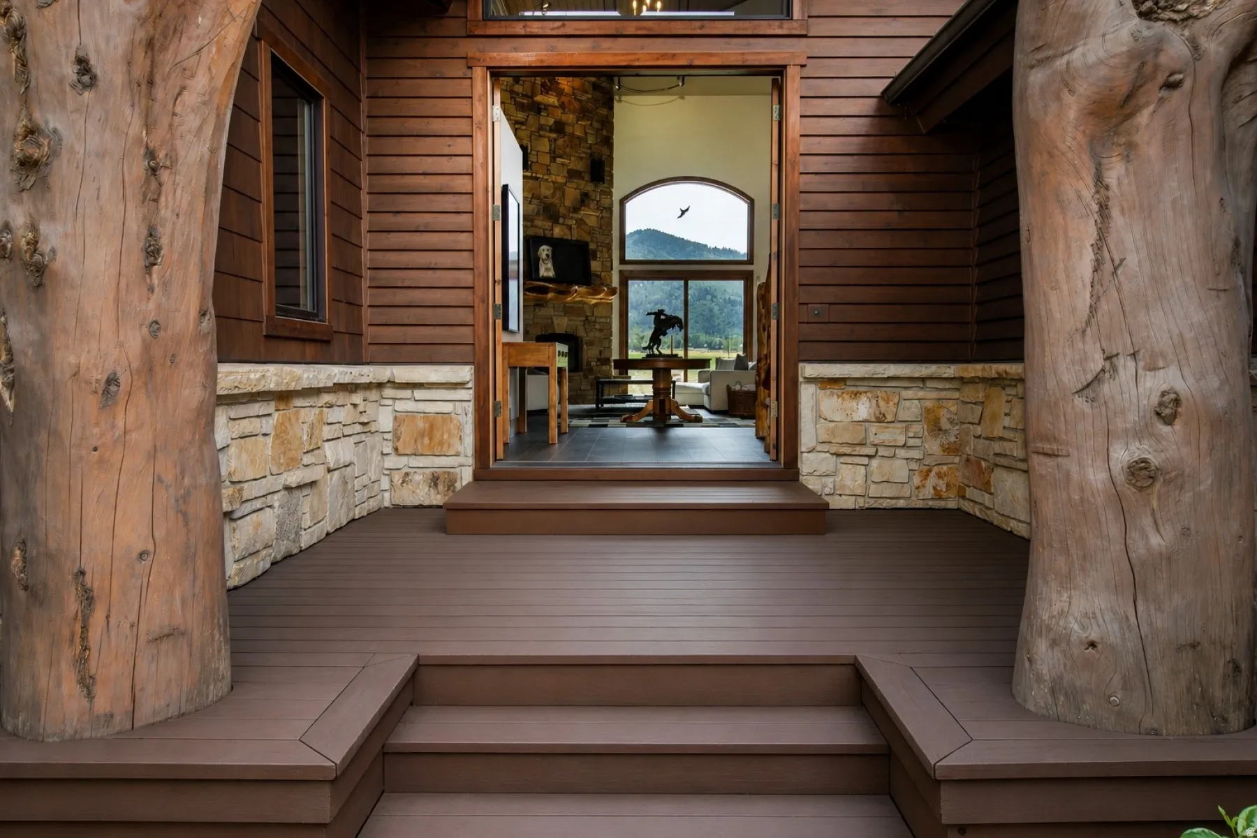 Exterior entryway featuring a multi-level composite deck, natural stone wainscoting, and large timber structural elements