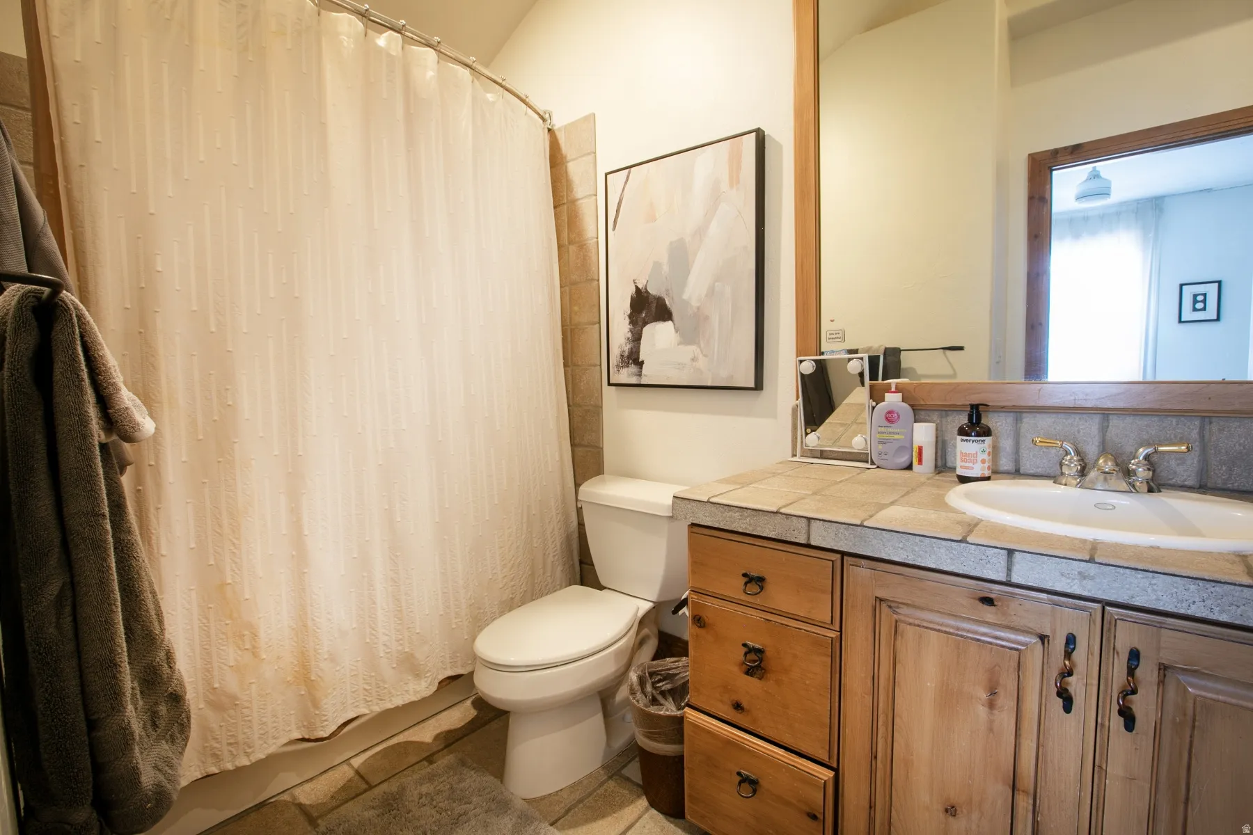 Bathroom featuring a tile-surround shower, wood-finish vanity with built-in cabinetry and drawers, and a tile countertop