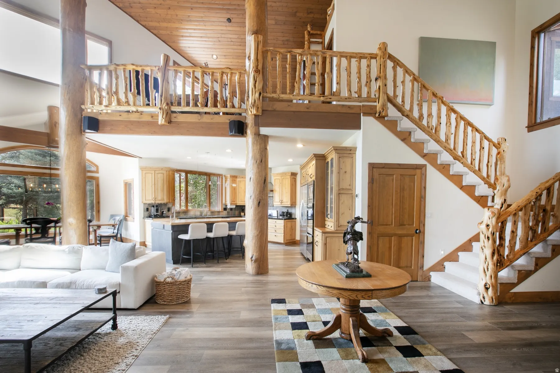 Spacious great room featuring natural wood columns and exposed beams, a multi-level staircase with log railings, and wood-finish flooring