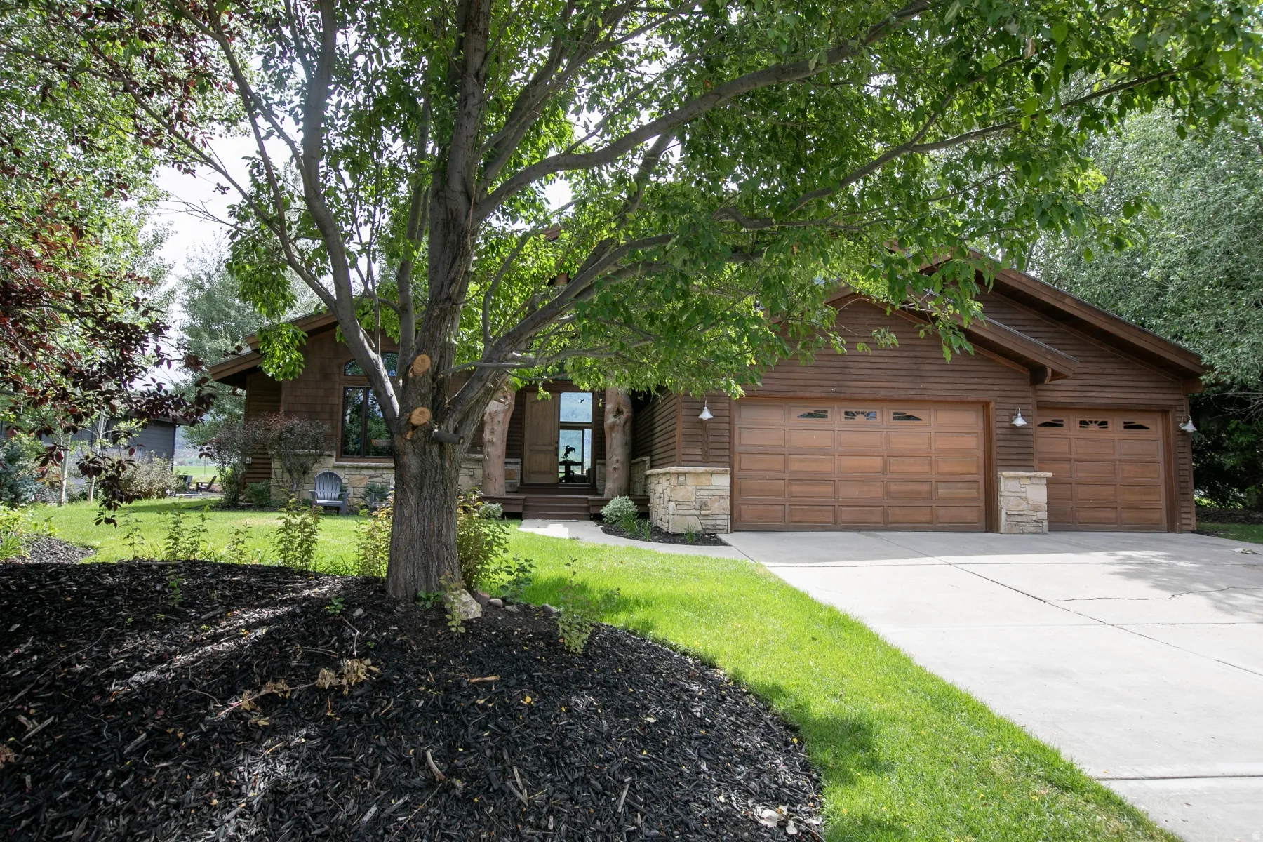 Wood-paneled facade with stone accents, a multi-car garage featuring wood-finish doors, and a concrete driveway