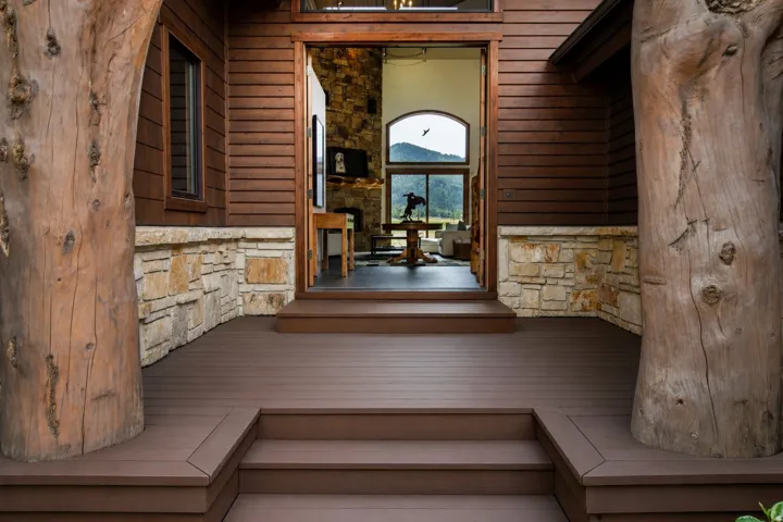 Exterior entryway featuring a multi-level composite deck, natural stone wainscoting, and large timber structural elements