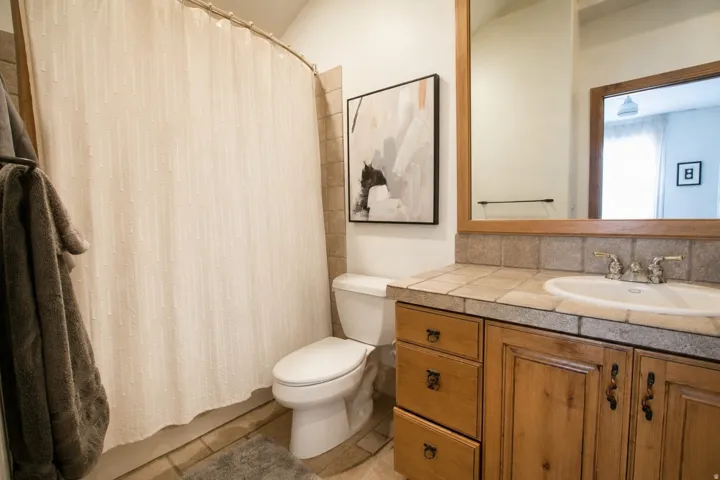 Bathroom featuring a wood-finish vanity with a tile countertop, integrated sink, and wall-mounted mirror