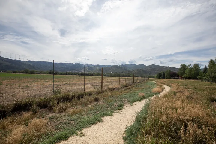 Expansive open field bordered by a wire fence and a winding dirt path