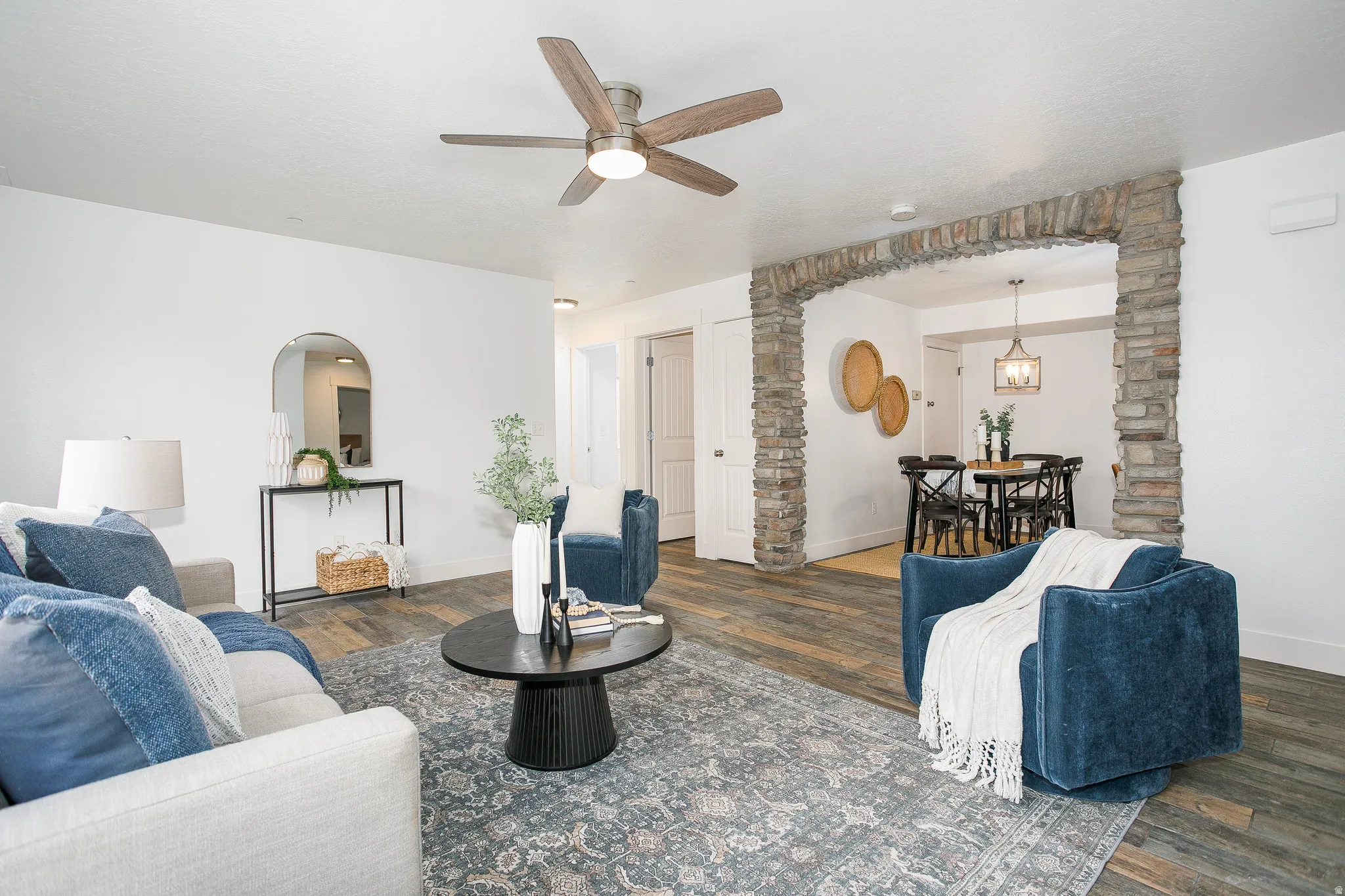 Spacious living area featuring wood-finish flooring, a ceiling fan, and a stone archway