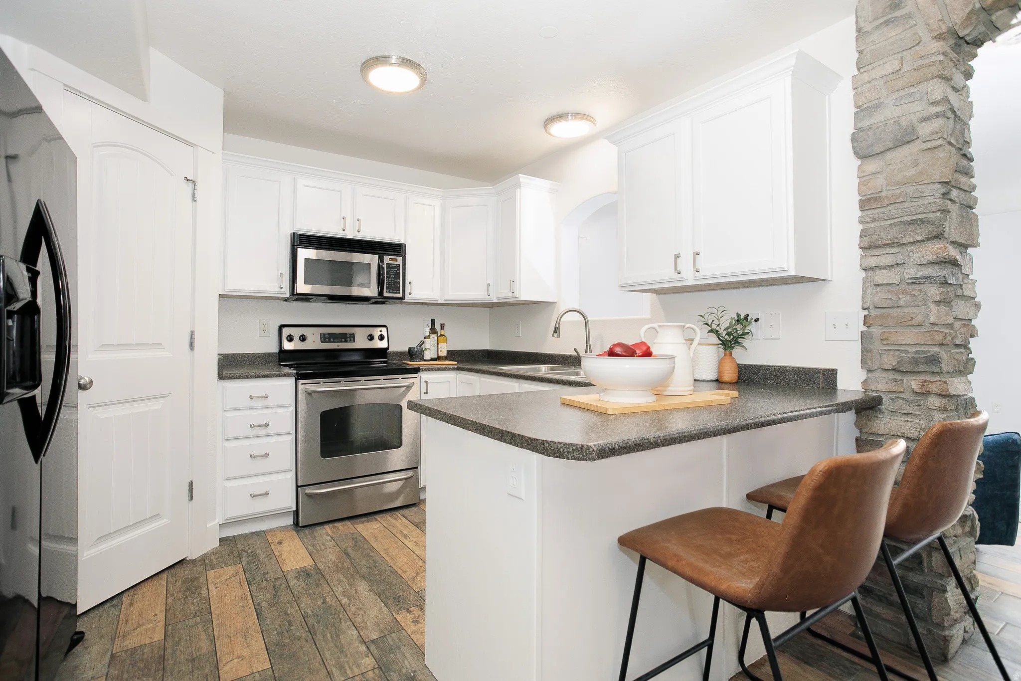 Modern kitchen featuring white cabinetry, stainless steel appliances, dark countertops, and wood-finish flooring
