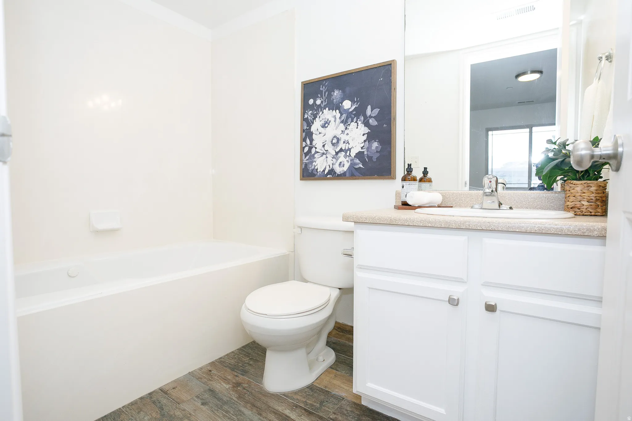 Full bathroom featuring a built-in tub, white vanity with cabinet storage, integrated sink, and wood-finish flooring