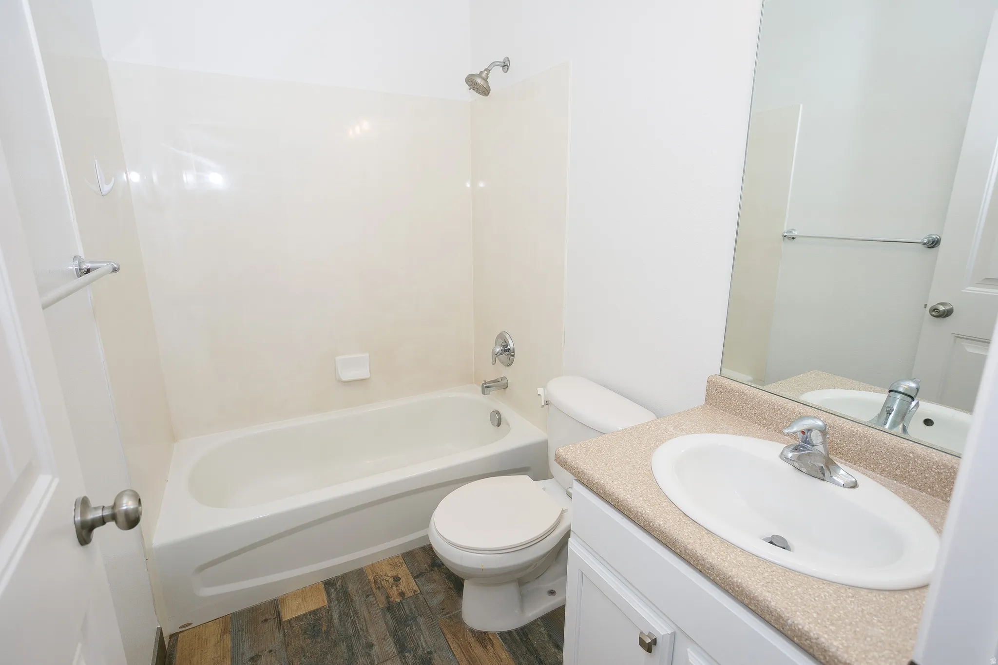 Full bathroom featuring a white porcelain tub with shower, wood-finish flooring, white vanity with a speckled countertop, integrated sink, and an expansive wall mirror