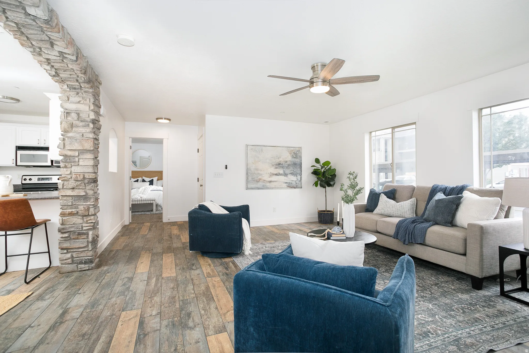 Spacious living area featuring wood-finish flooring, a stone-clad architectural column, and abundant natural light from multiple windows