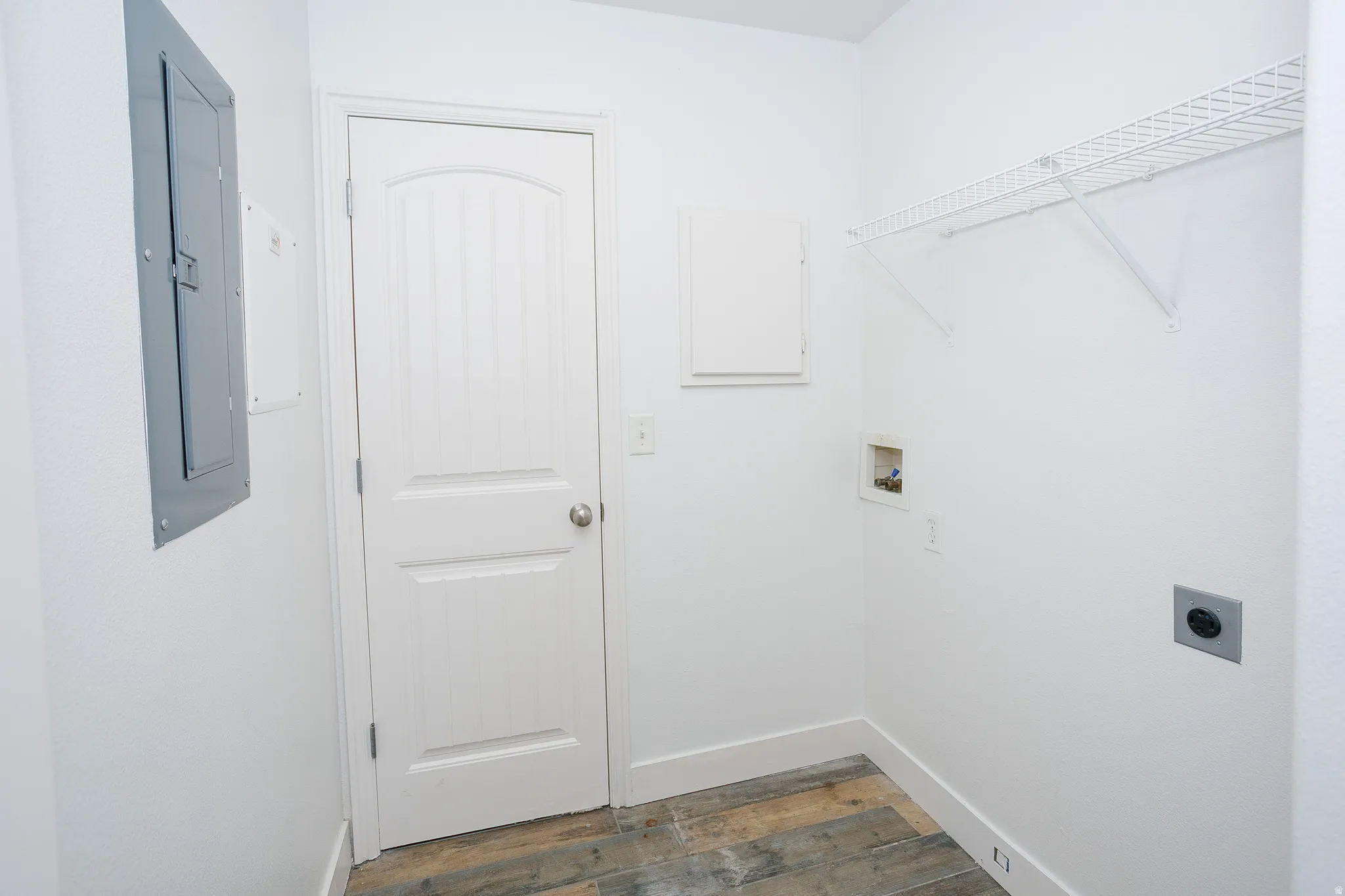 Utility room featuring wood-finish flooring, white walls, and a white wired shelving unit