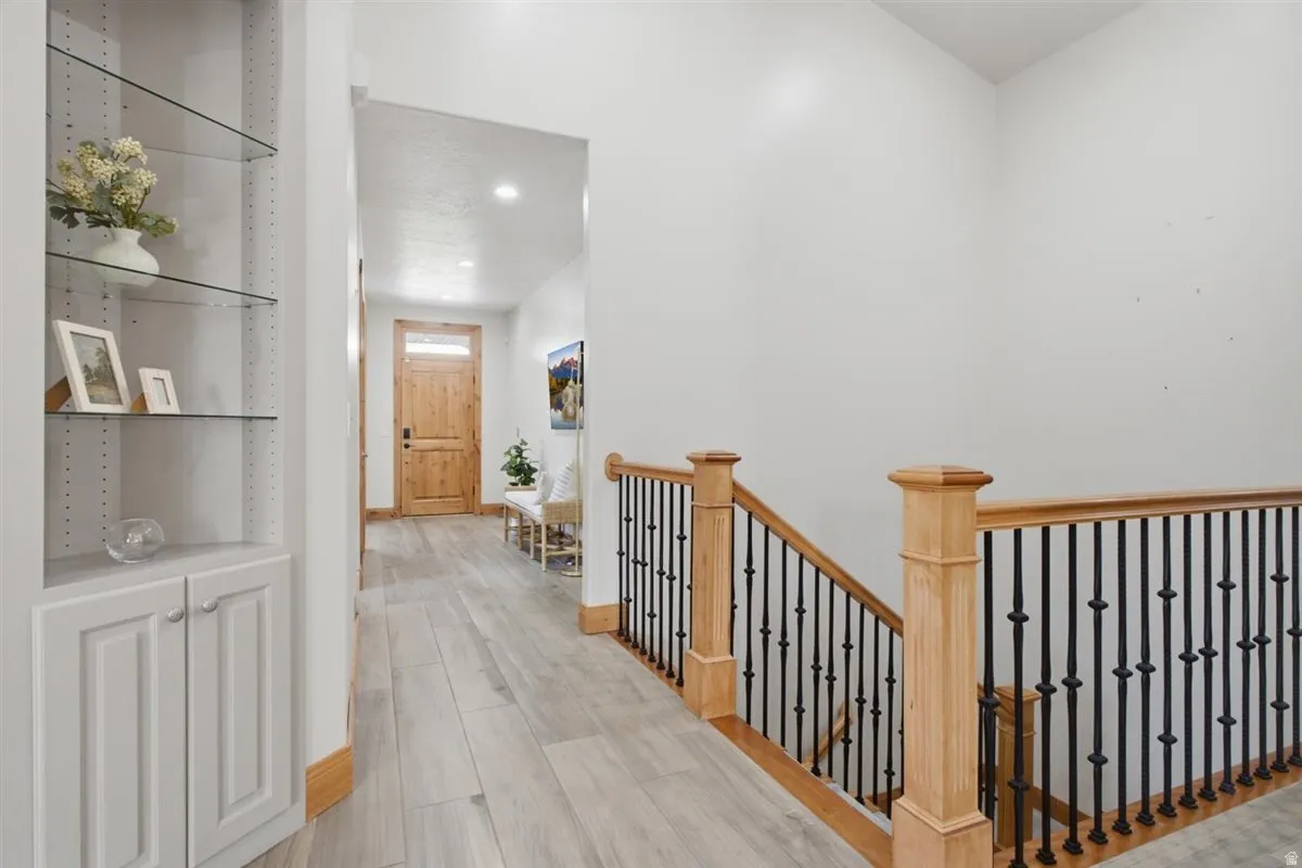 Entryway featuring wood-finish flooring, a built-in shelving unit with glass shelves and base cabinetry, a natural wood entry door with transom window, and a natural wood staircase with wrought iron balusters