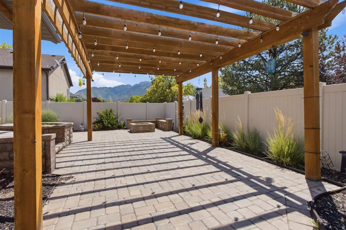 Expansive paver patio featuring a wooden pergola with string lighting