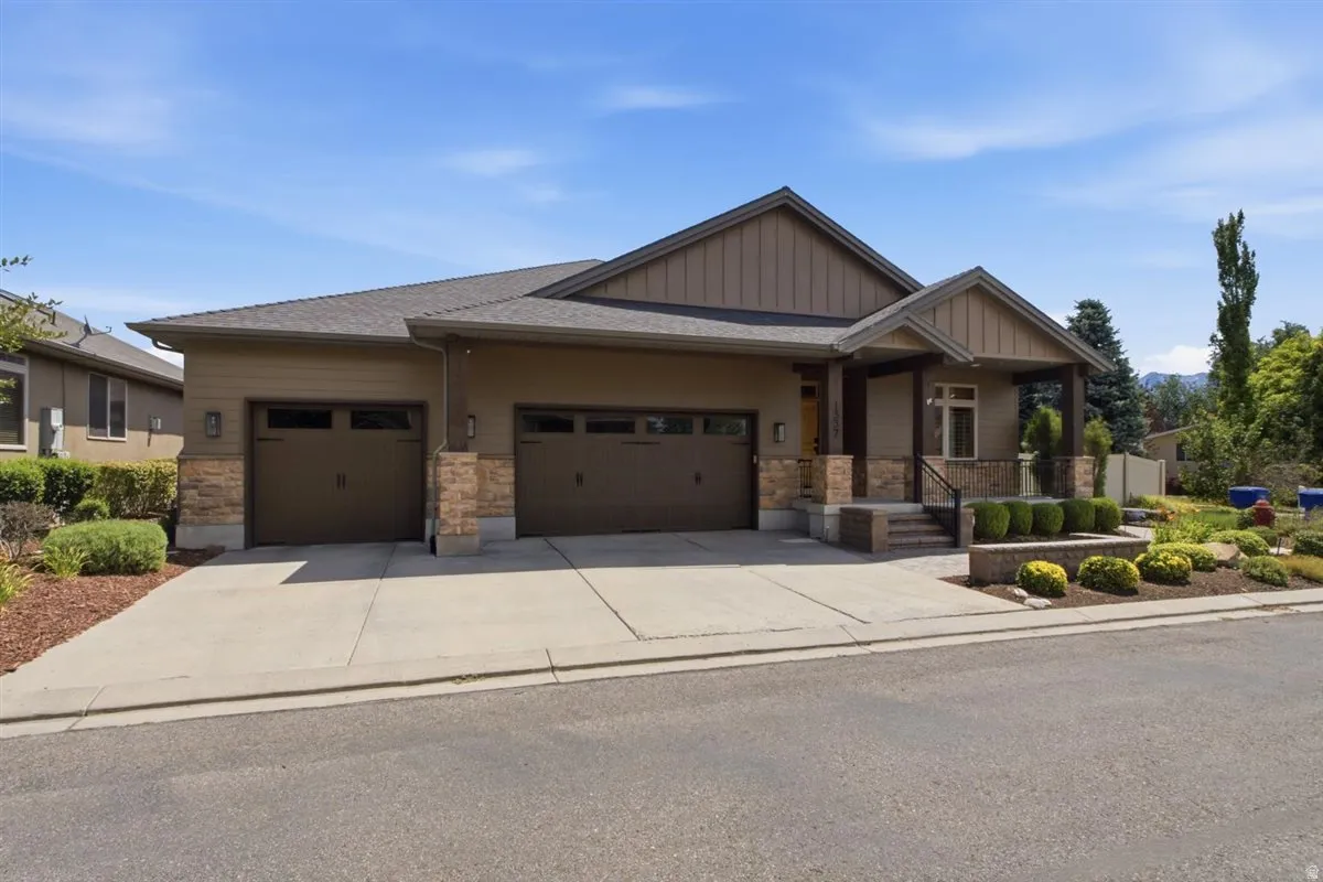 Contemporary residence featuring a covered entry, stone veneer accents, two-car garage with individual doors, concrete driveway, and established landscaping