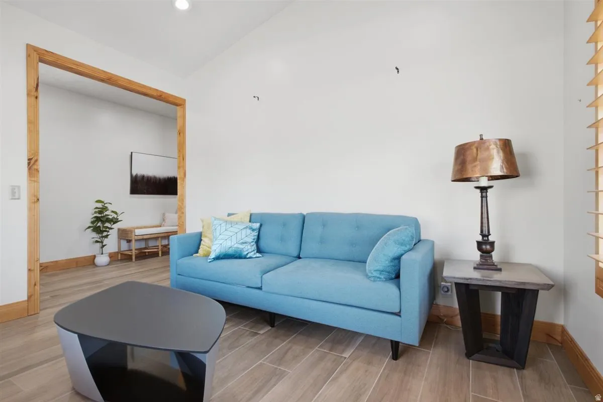 Vaulted ceiling living area featuring wood-finish flooring, a wood-framed entryway, and natural light from visible window blinds