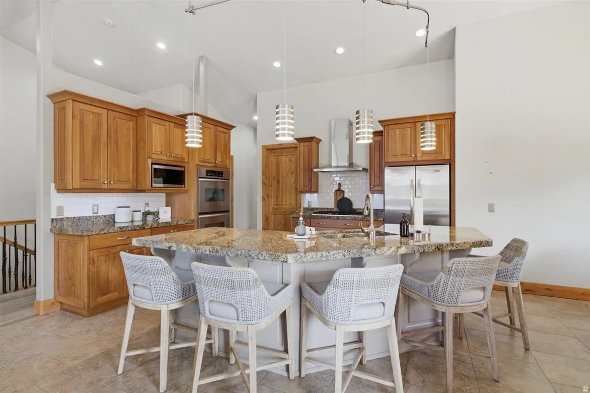 Kitchen featuring an expansive center island with seating, a stainless steel appliance suite, wood cabinetry, granite countertops, and a subway tile backsplash