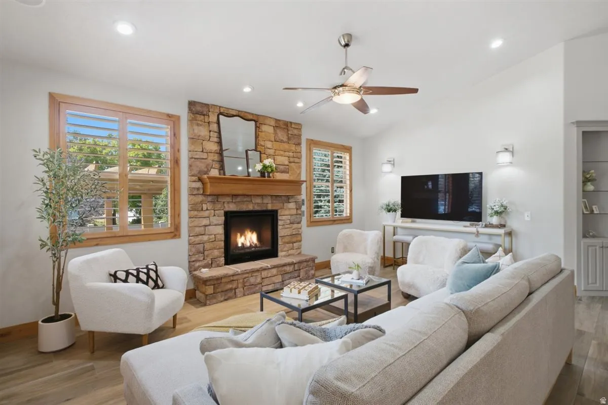 Inviting living room showcasing a wood-burning fireplace with brick surround and mantel, complemented by recessed ceiling lighting and a ceiling fan