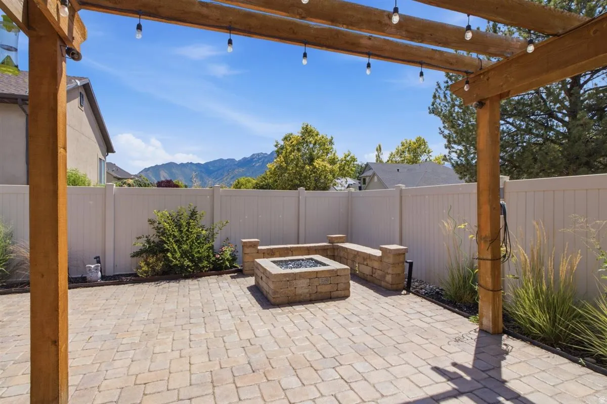 Paver patio featuring a stone fire pit with integrated stone seating, a wooden pergola with string lighting, and a privacy fence